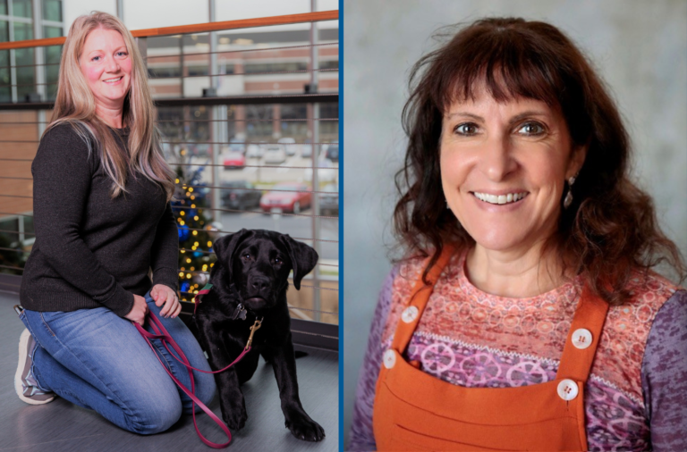 Woman smiling with black dog on leash indoors, alongside another woman in colorful attire.